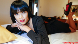 Exotic Ladyboy lays in bed wearing black dress and pumps
